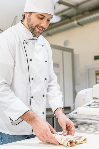 Panadero en uniforme de chefs blancos amasando masa en la mesa de panadería - foto de stock