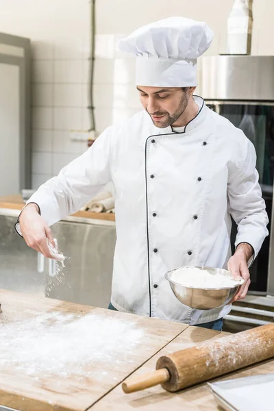 Pâte de cuisson uniforme Baker in white chefs sur table en bois — Photo de stock