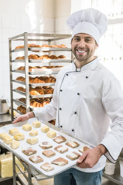 Smiling baker with tray of uncooked dough in bakehouse — Stock Photo