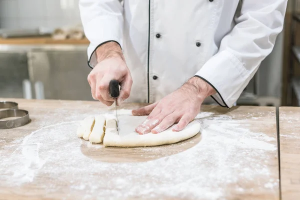 Gros plan des mains de boulanger couper la pâte sur une table en bois — Photo de stock