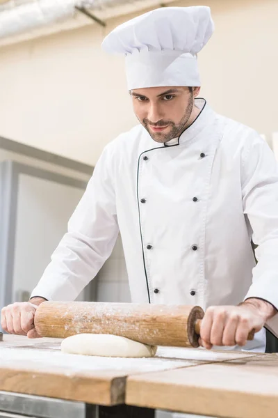 Chef rolling out dough with rolling pin on wooden table — Stock Photo