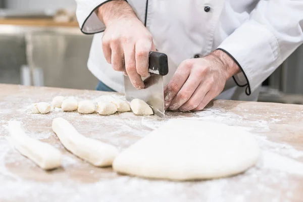 Großaufnahme der Hände von Köchen, die Teig mit Ausstecher auf Holztisch trennen — Stockfoto