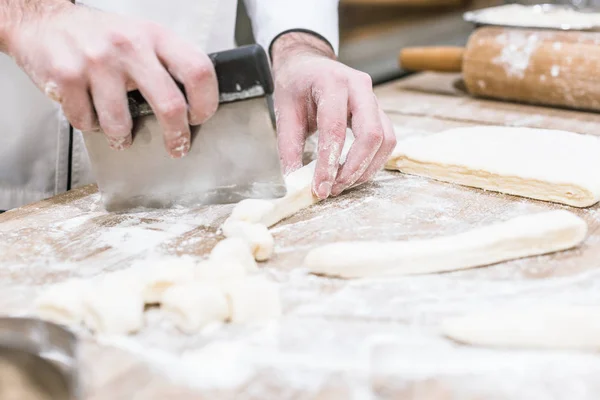 Gros plan des mains de boulanger couper la pâte sur une table en bois — Photo de stock