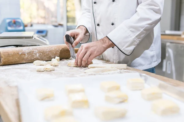 Vue recadrée des mains de boulanger coupant la pâte sur la table — Photo de stock