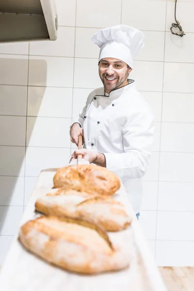 Chef sorrindo tirando pães na padaria — Fotografia de Stock