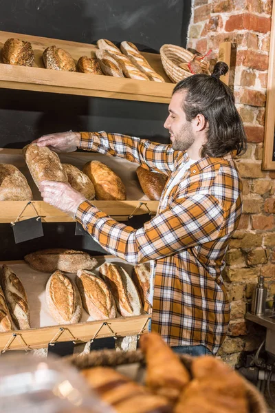 Side view of male seller putting freshly baked bread on wooden shelf — Stock Photo