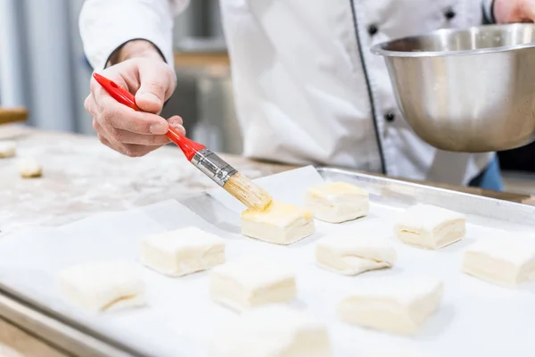 Male hand of chef oiling dough with basting brush in kitchen — Stock Photo