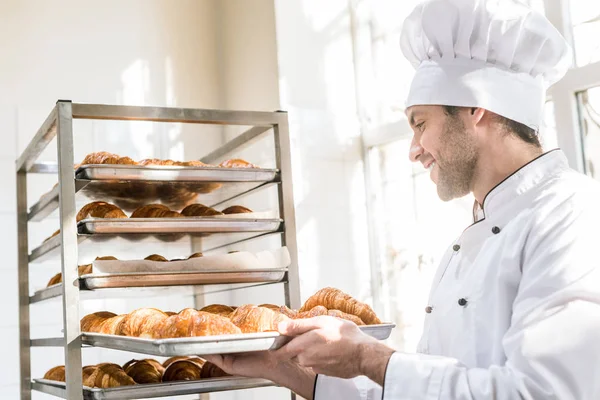 Side view of smiling baker taking tray with pastry — Stock Photo