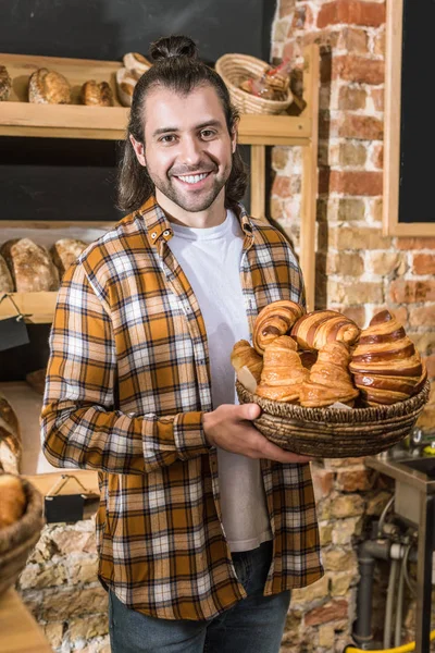 Vendedor sorrindo segurando cesta de vime com pastelaria em padaria — Fotografia de Stock