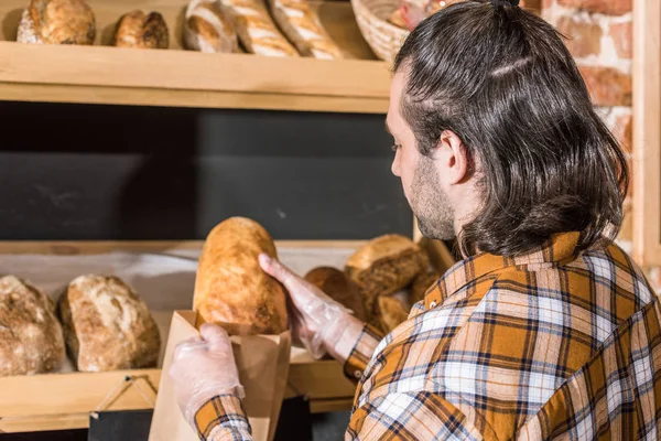 Male seller putting fresh bread in paper bag — Stock Photo