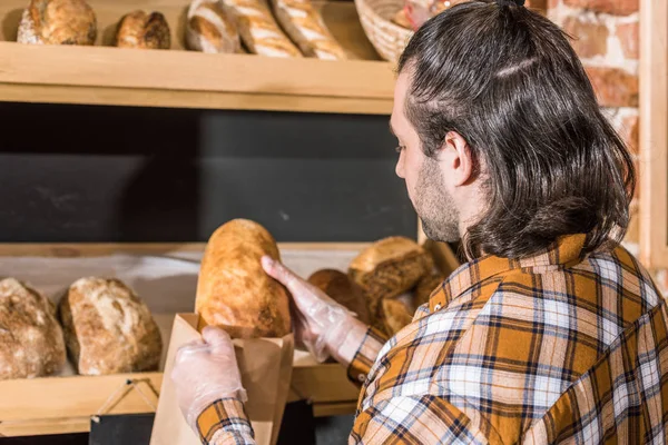 Vendedor masculino colocando pão fresco em saco de papel — Fotografia de Stock