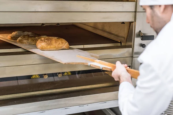 Male baker taking out freshly baked bread — Stock Photo
