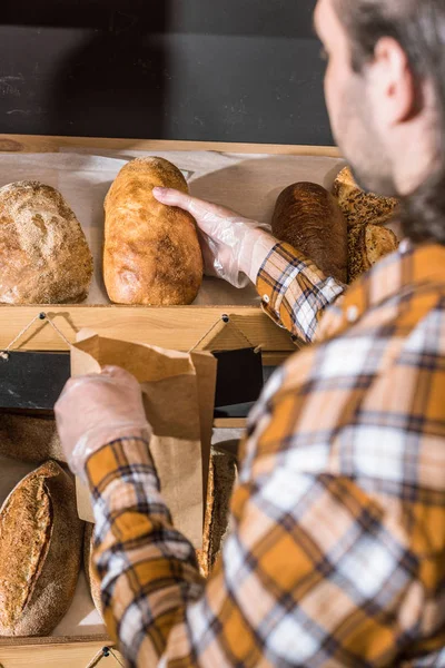 Продавец мужского пола берет в руки свежеиспеченный хлеб — стоковое фото