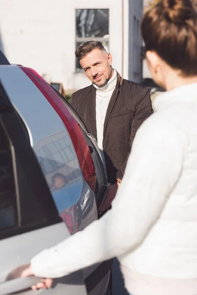 Femme ouvrant la porte de la voiture et homme regardant et souriant dans la rue — Photo de stock