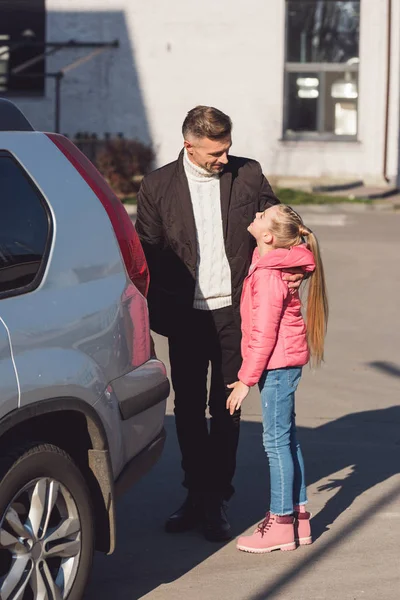 Дочь смотрит на папу и улыбается возле машины. — стоковое фото
