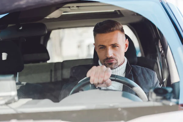 Handsome man sitting in car and holding steer — Stock Photo