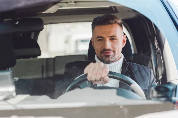 Cheerful man sitting in car and holding steer — Stock Photo