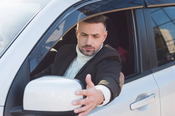 Hombre guapo mirando en el espejo y sentado en el coche - foto de stock