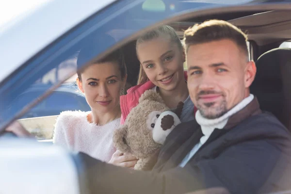 Preteen daughter sitting in car with teddy bear and parents — Stock Photo