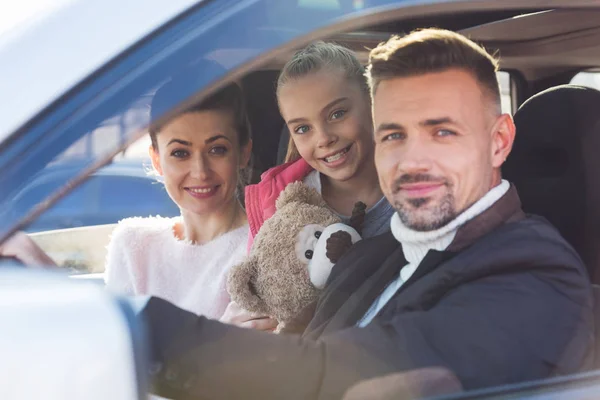 Hija preadolescente sentada en coche con oso de peluche, mamá y papá — Stock Photo