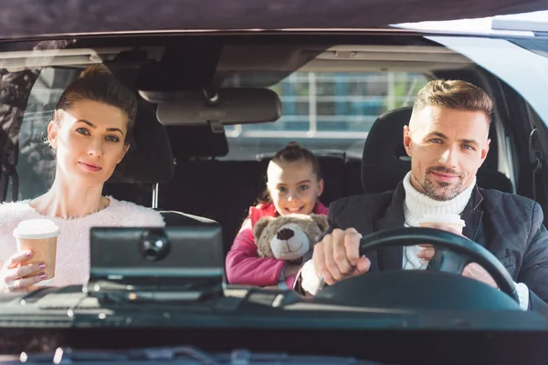 Maman et papa assis dans la voiture avec sa fille et tenant des tasses en papier — Photo de stock