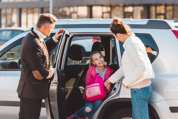 Hija preadolescente sentada en coche con puerta abierta cerca de perents - foto de stock