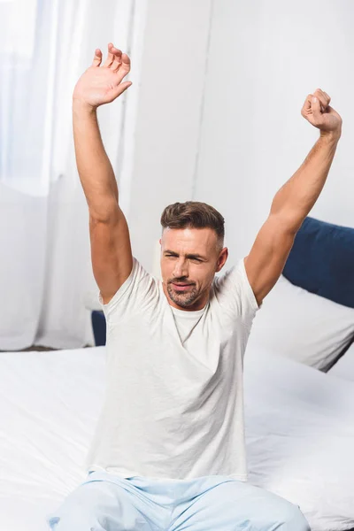 Schläfriger Mann sitzt auf Bett und gähnt — Stockfoto