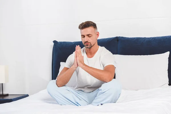 Bonito homem praticando ioga na cama — Fotografia de Stock