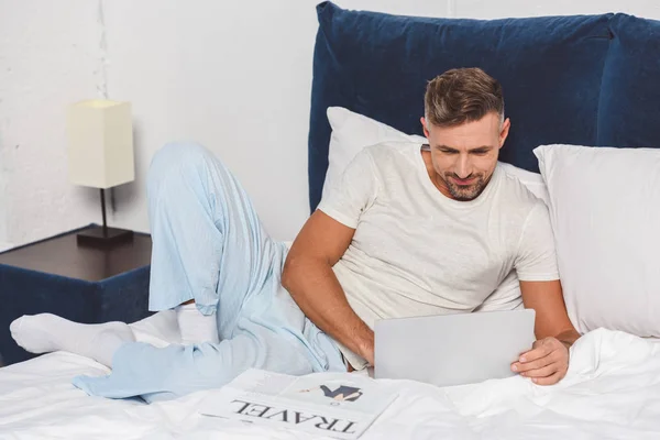 Bello uomo che utilizza il computer portatile e sdraiato a letto — Foto stock