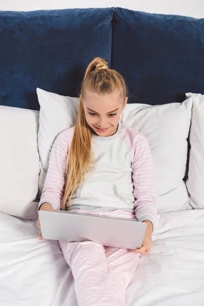 Happy preteen kid lying in bed with laptop — Stock Photo