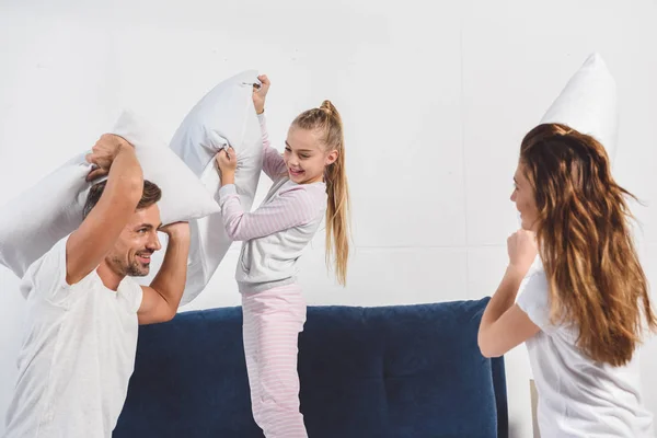 Alegres padres teniendo pelea de almohadas con su hija en el dormitorio - foto de stock