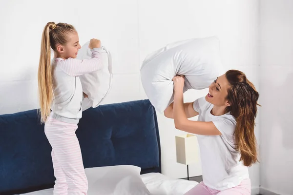 Весёлые мама и дочь дерутся на подушках дома — стоковое фото