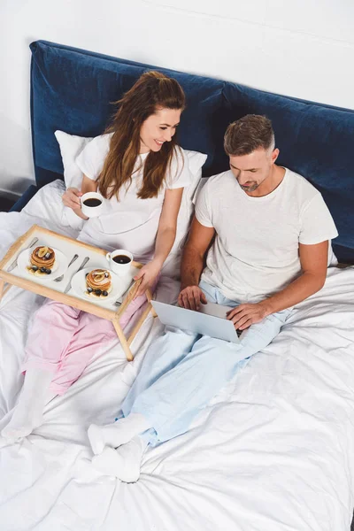 Husband using laptop while wife having breakfast — Stock Photo