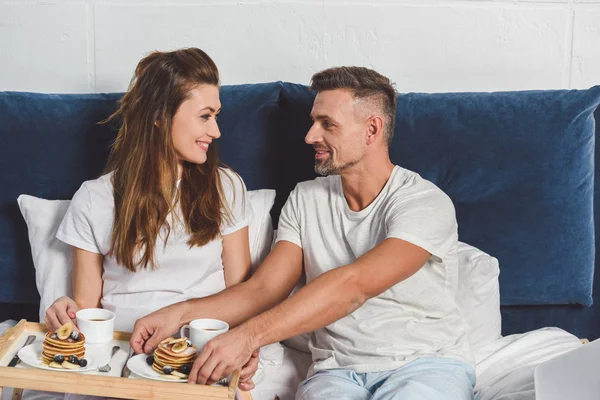 Couple souriant se regardant tout en prenant le petit déjeuner au lit — Photo de stock