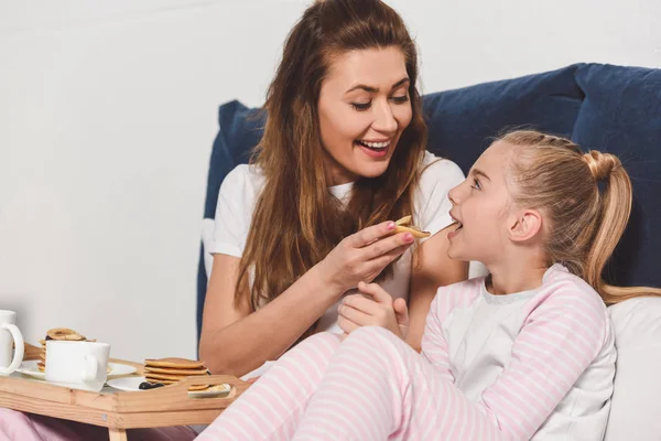 Усміхнена мати годує дочку в ліжку під час сніданку — стокове фото