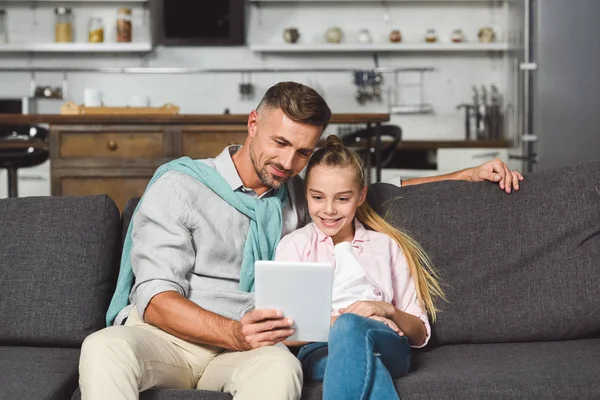 Father and daughter sitting on sofa and using digital tablet — Stock Photo