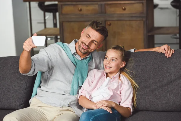 Lächelnde Tochter und Vater machen Selfie im Smartphone, während sie auf dem Sofa sitzen — Stockfoto
