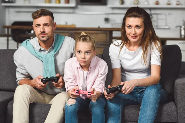 Família concentrada sentada no sofá e jogando videogame — Fotografia de Stock