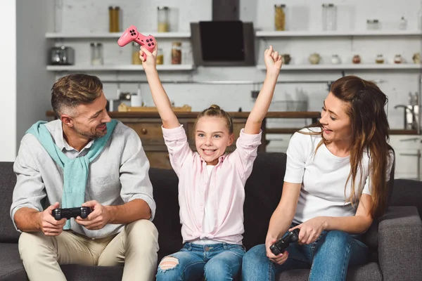 Счастливая дочь радуется победе, играя в видеоигры с родителями — стоковое фото