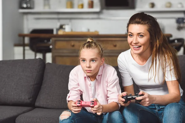 Концентрована дочка грає у відеогру з усміхненою матір'ю — стокове фото