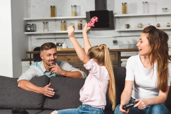 Happy daughter rejoicing victory in video game while father sitting behind sofa — Stock Photo