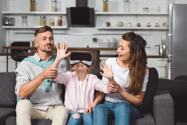 Daughter sitting on sofa in virtual reality headset with parents — Stock Photo