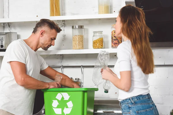 Adult couple putting empty plastic bottles in green box with recycle sign — Stock Photo