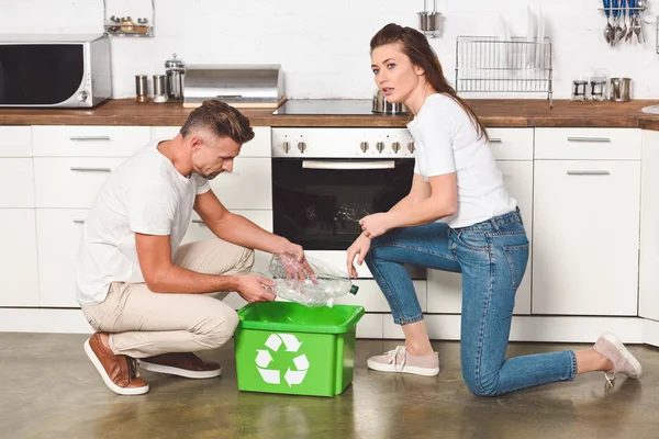 Взрослая пара кладет пустые пластиковые бутылки в утилизации зеленой коробке на кухне — стоковое фото