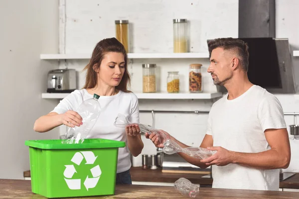 Husband and wife standing at kitchen and putting empty plastic bottles in recycle box — Stock Photo