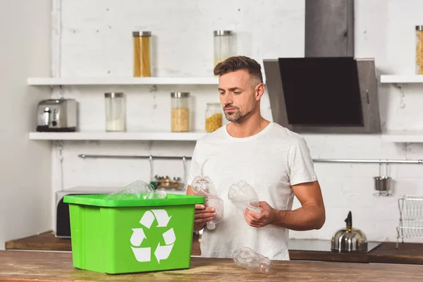 Uomo adulto in possesso di bottiglie di plastica con scatola di riciclaggio verde in cucina — Foto stock