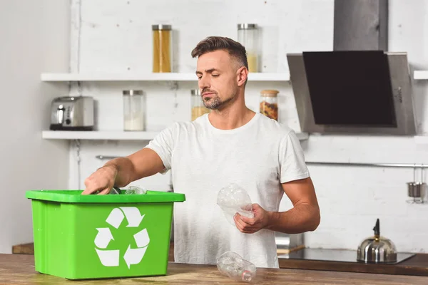 Hombre guapo poniendo botellas de plástico en caja de reciclaje verde - foto de stock