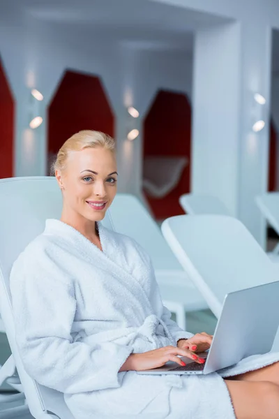 Красива жінка, що друкує на ноутбуці в білому халаті — стокове фото
