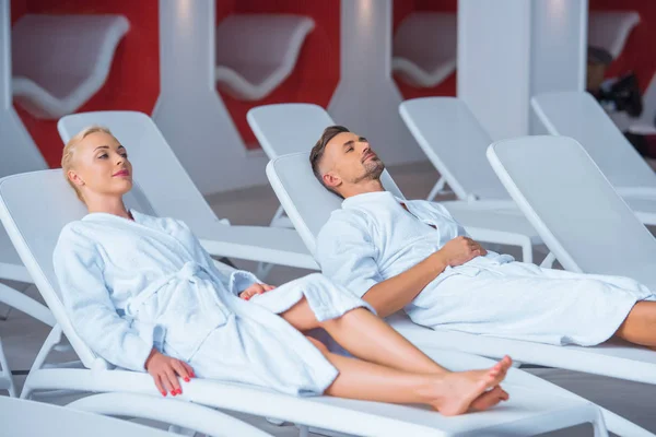 Couple reposant sur des chaises longues en peignoirs blancs — Photo de stock