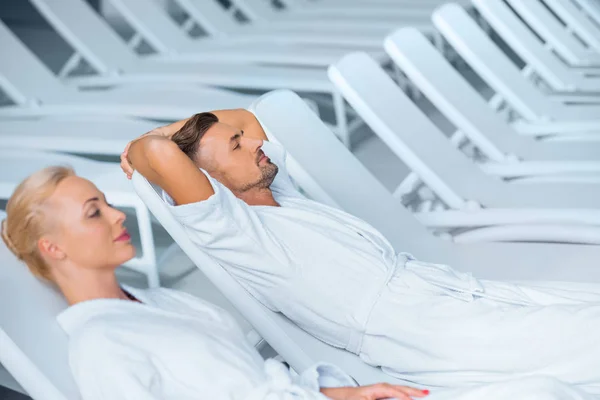 Casal relaxante em espreguiçadeiras em roupões brancos — Fotografia de Stock